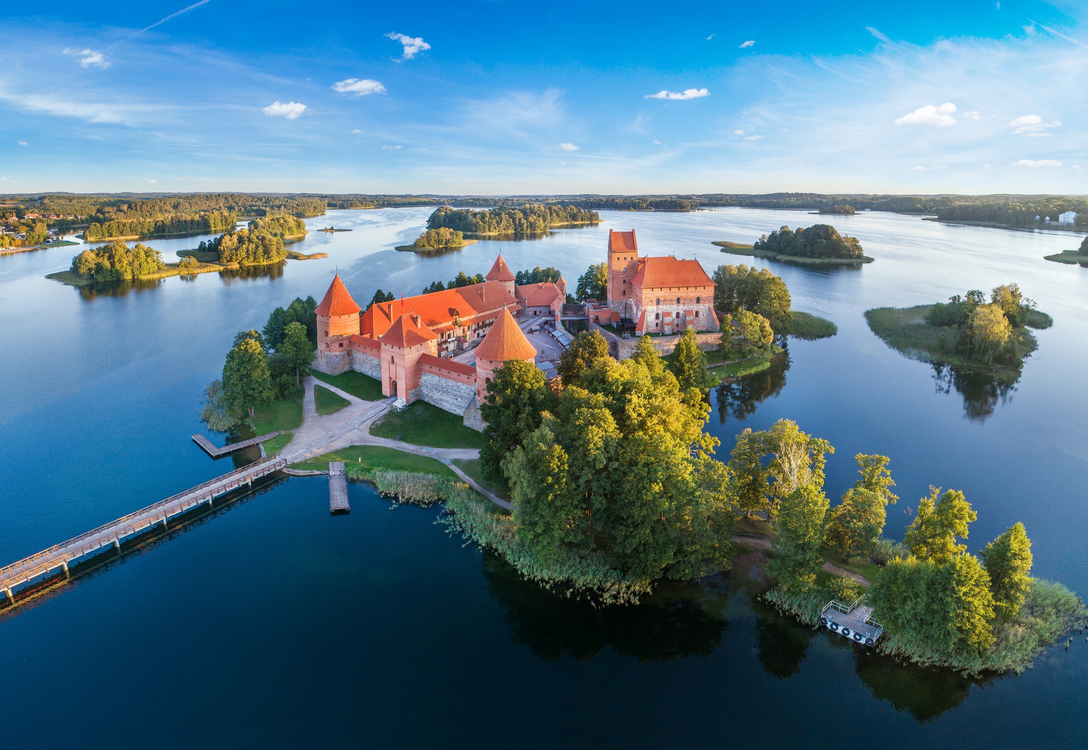 Vue aérienne d’un grand château historique Estonien en briques rouges entouré d’eau. Le château est situé sur une île, reliée au continent par un pont étroit. Le paysage environnant comprend plusieurs petites îles et de vastes voies navigables.